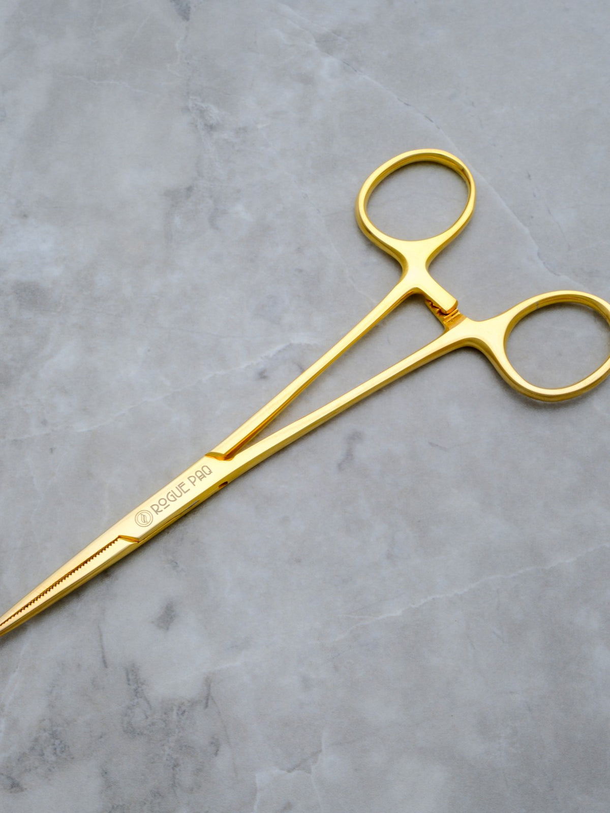 A pair of Rogue Paq gold-toned hemostat jay-clips. The surgical-grade stainless steel tools feature a high-shine gold finish and a locking mechanism, repurposed as a sophisticated accessory for packing or holding hand-rolled joints.
