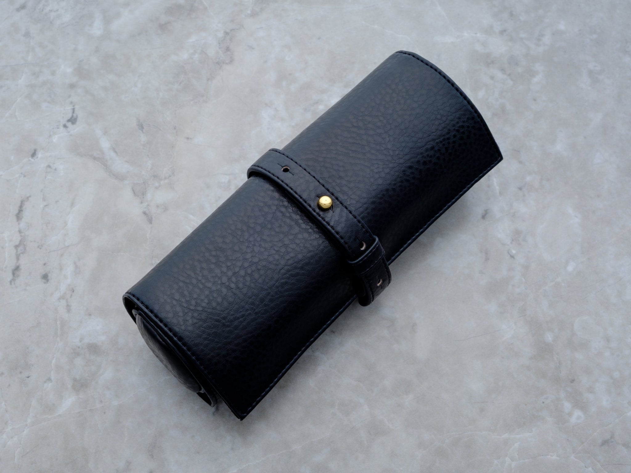 A studio shot of the Rogue Paq Vegan Leather Ritual Case rolled horizontally against a gray marble background. The clean lines and uniform pebbled texture highlight the professional craftsmanship of this scent-suppressant stash bag.