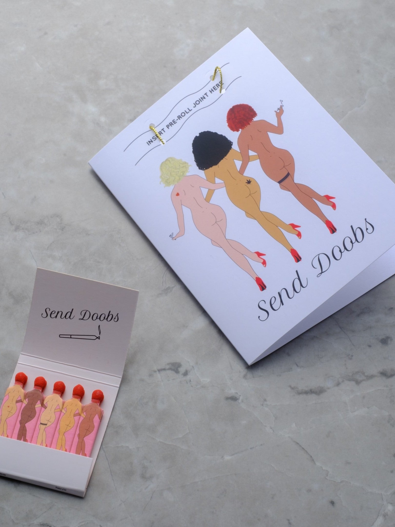 Rogue Paq x Kush Kards 'Send Doobs' greeting card featuring a built-in slot for holding a pre-rolled joint; styled with matching vintage-style SendNudes matches for a complete cannabis lover's gift set.