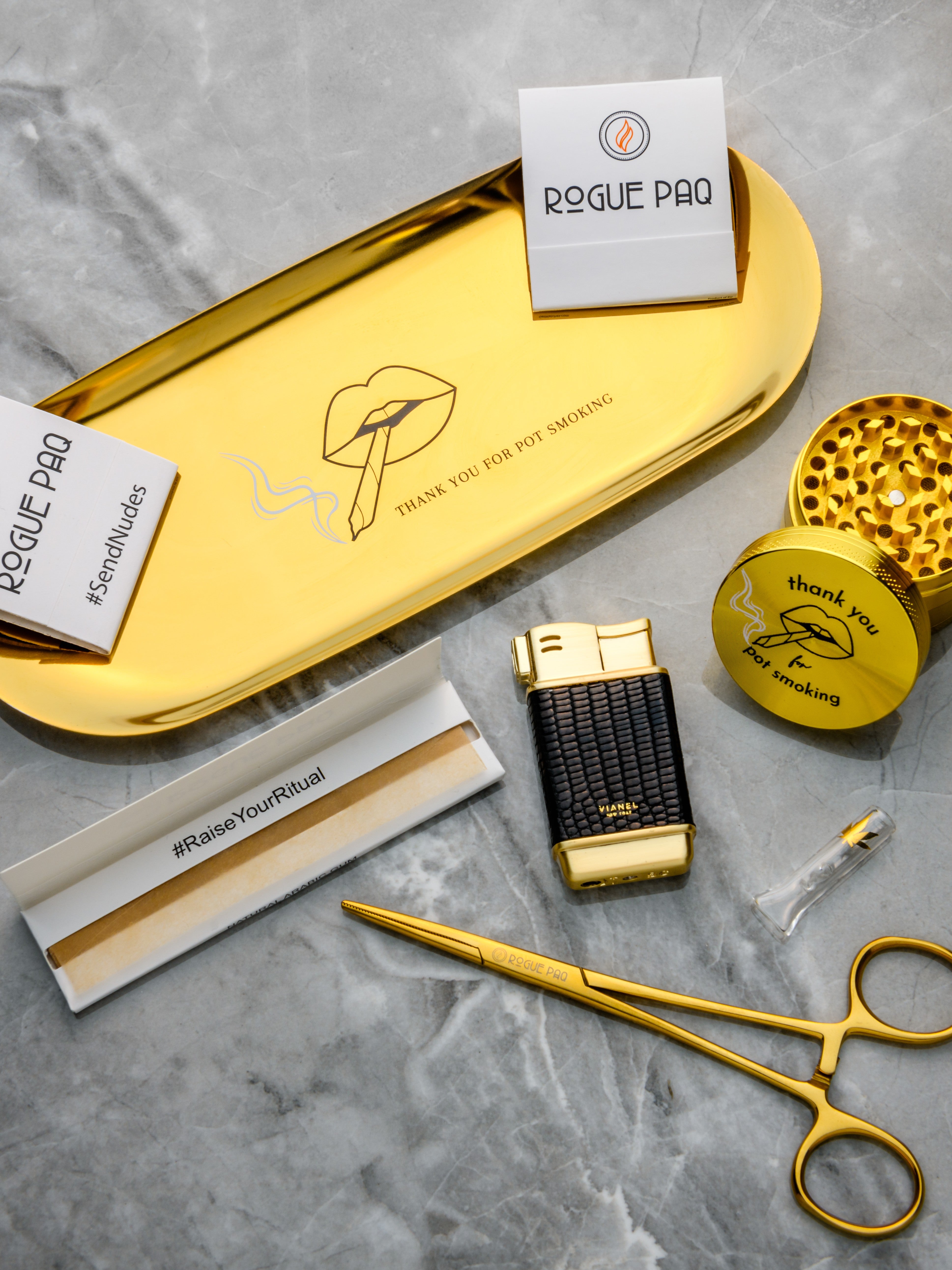Rogue Paq Thank You for Pot Smoking Gift Set featuring a gold-tone stainless steel rolling tray and matching grinder; a complete vintage-inspired cannabis ritual kit which also includes two books of SendNudes matches, a glass tip, rolling papers, and hemostat joint clips.
