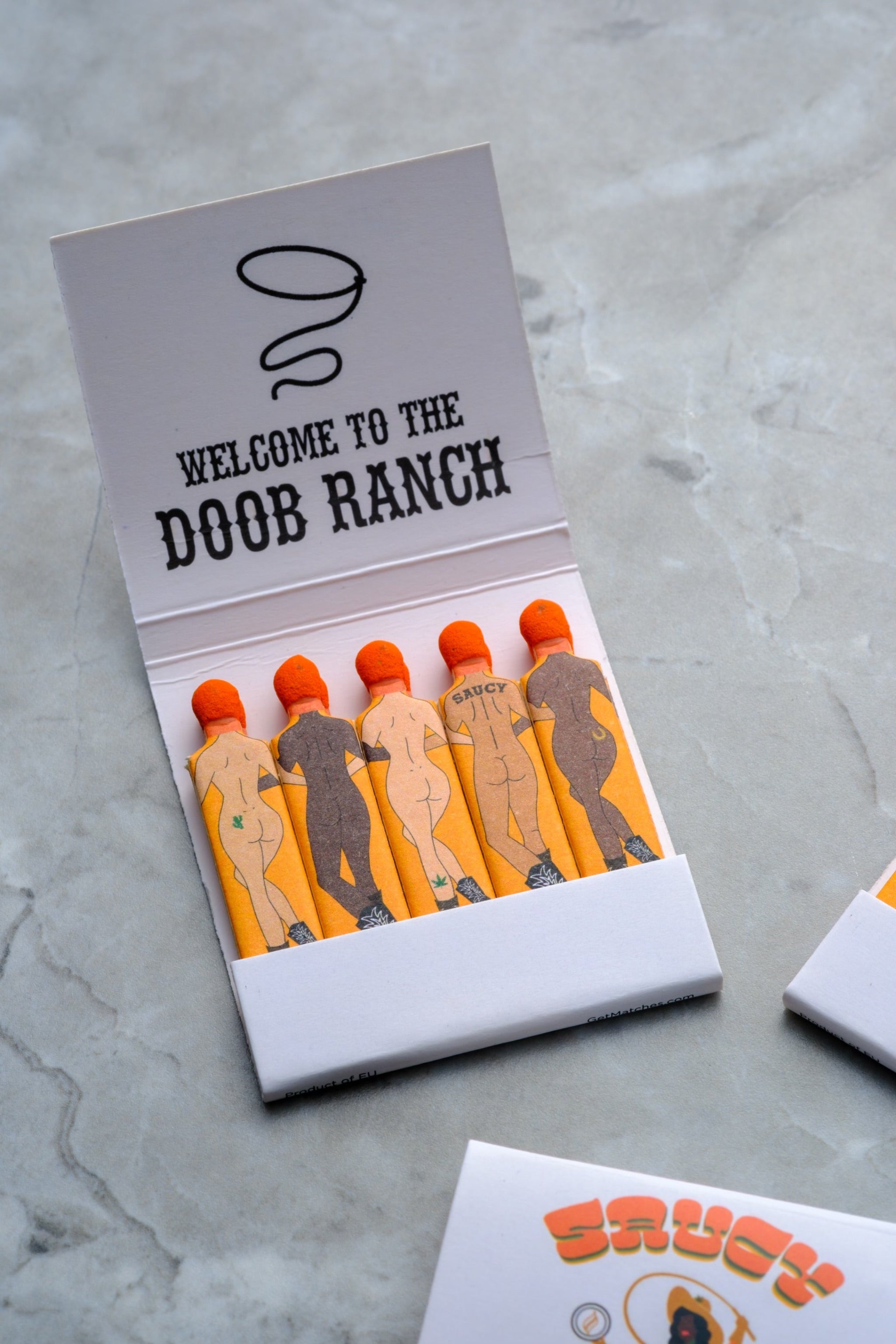 Close up of Send Nudes Doob Ranch matches focusing on small cowboy and cowgirl figures. These matches are perfect for gifting and for elevating your ritual.