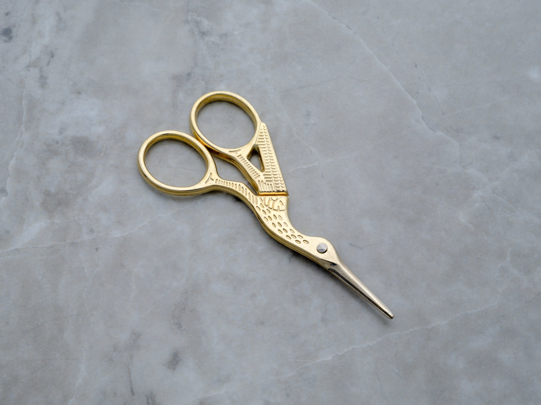 A pair of gold-toned precision trim scissors designed in the shape of a crane. The body of the bird forms the handles, while the long, slender beak serves as the sharp, stainless steel blades, finished in a high-polish gold for a luxury aesthetic.