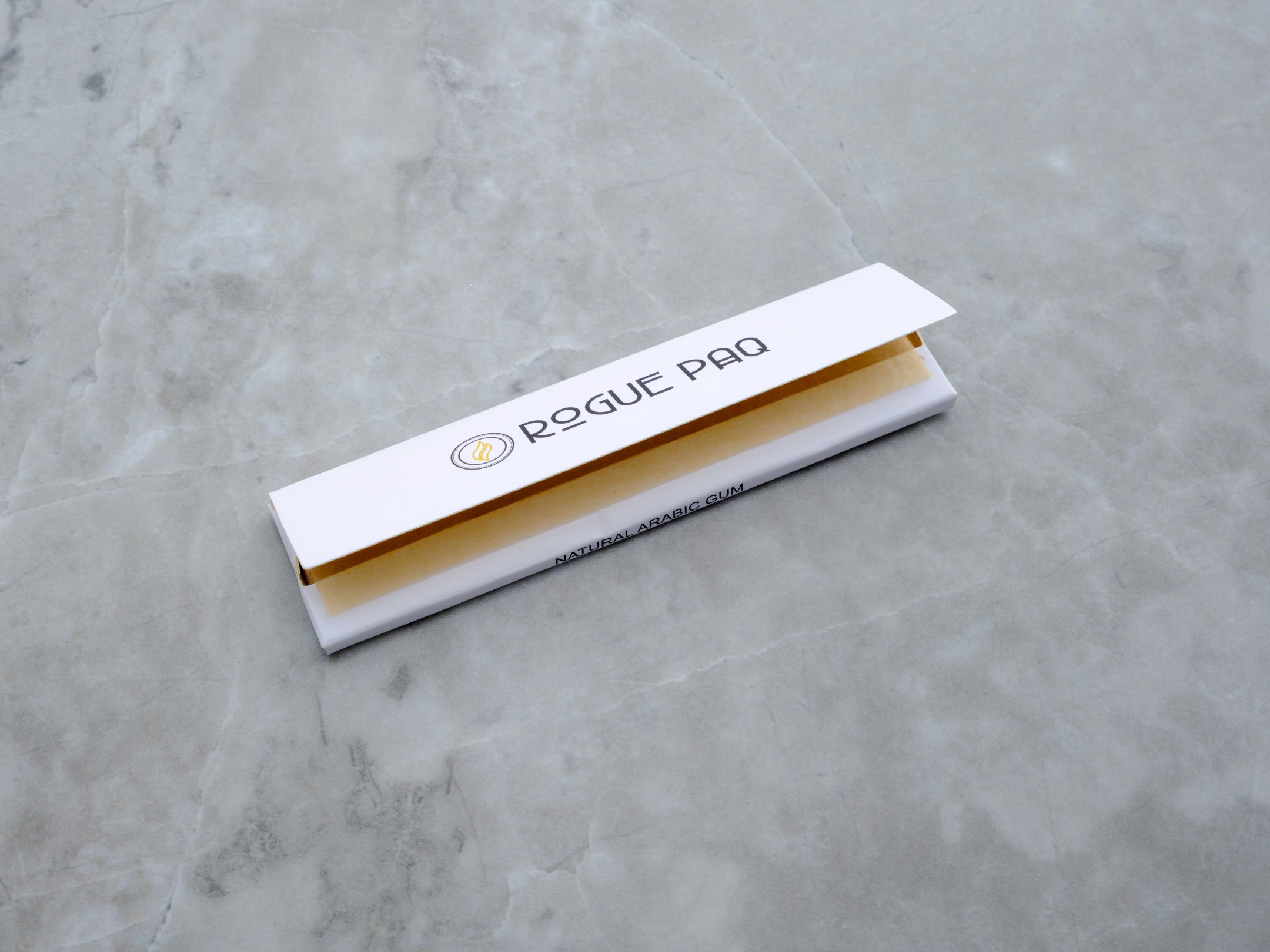 A lead shot of the Rogue Paq Signature King Slim rolling papers. The booklet features a sleek white cover with minimalist black branding. A single, unbleached brown hemp paper is pulled forward, showcasing its natural, additive-free texture and king slim dimensions