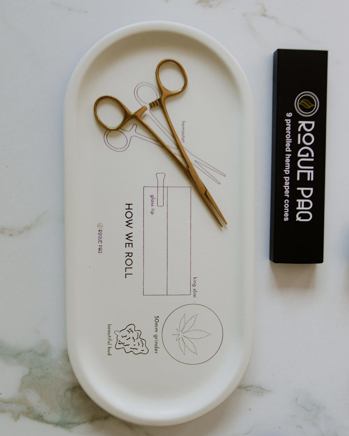 How We Roll porcelain tray styled with gold hemostat packing tool and hemp cones; an elegant rolling station that combines instructional art with premium functionality