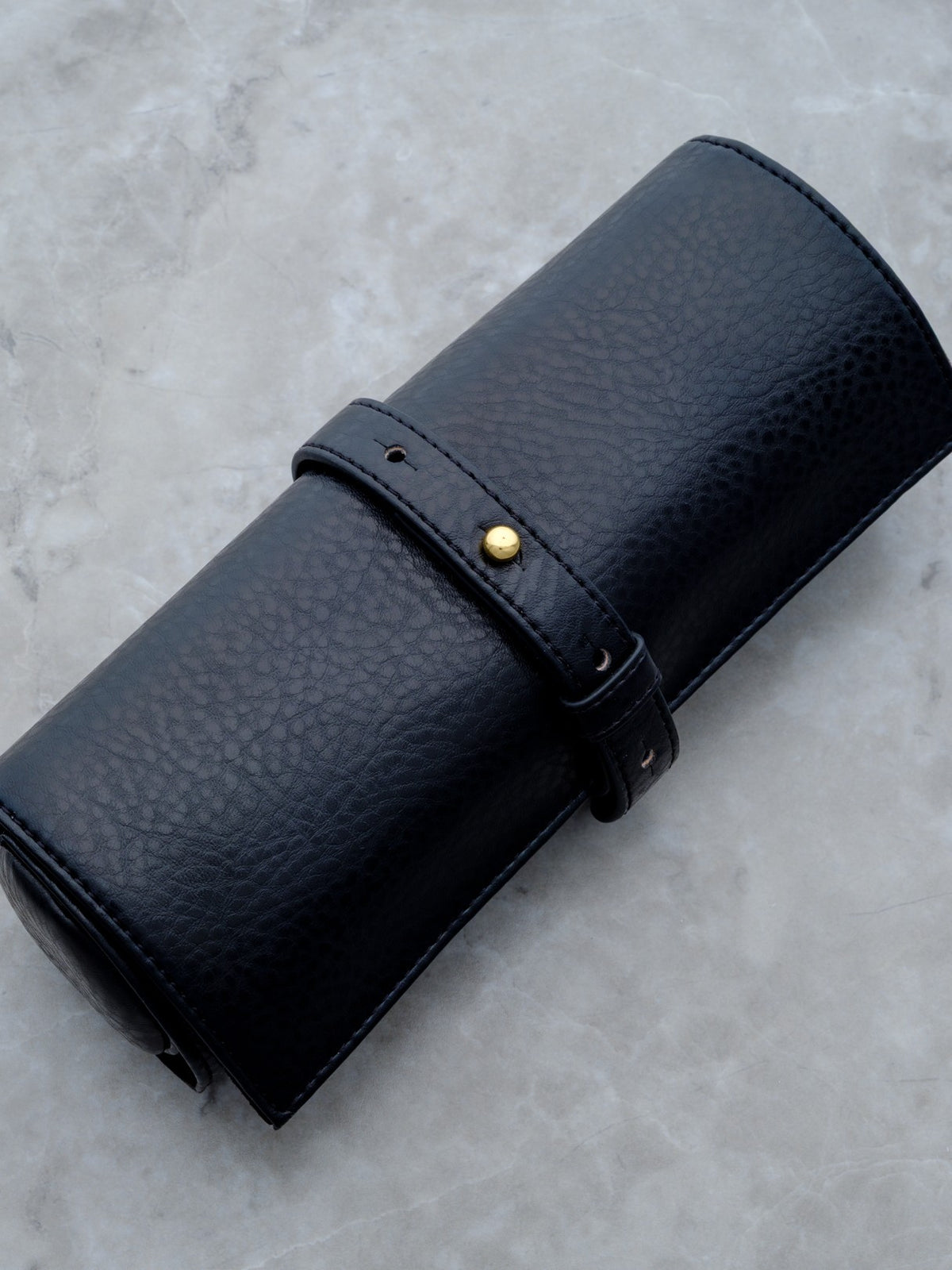 The Rogue Paq Vegan Leather Ritual Case shown in its compact, rolled position. The black pebbled vegan leather has a subtle sheen, secured by a minimalist wrap-around strap and gold-toned hardware, offering a discreet and high-end look.