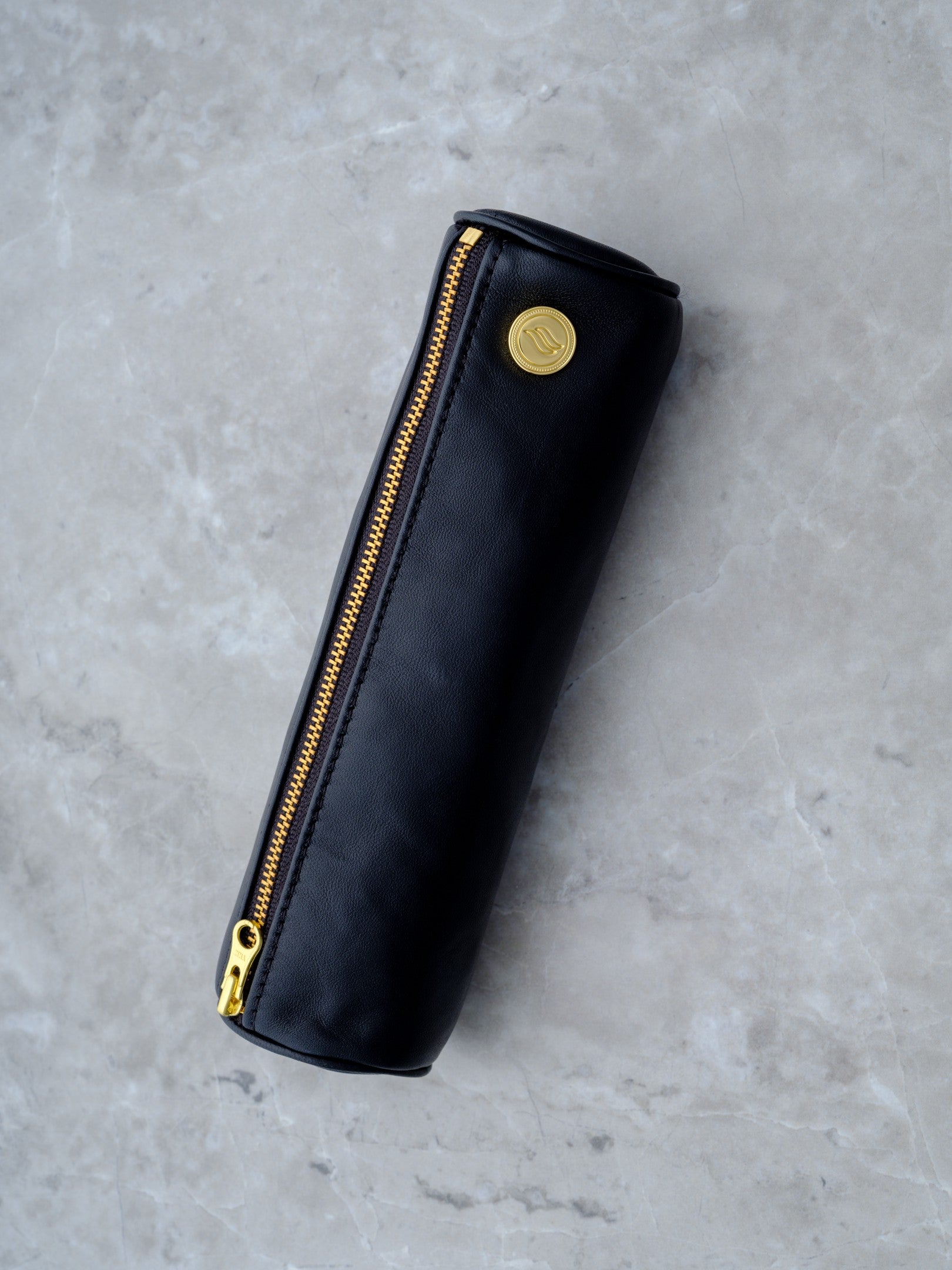 A side-profile shot of the Rogue Paq Solo Paq in premium black lambskin. The case has a sleek, tube-like silhouette and features high-quality gold-toned hardware, presenting a discreet and sophisticated aesthetic for travel.