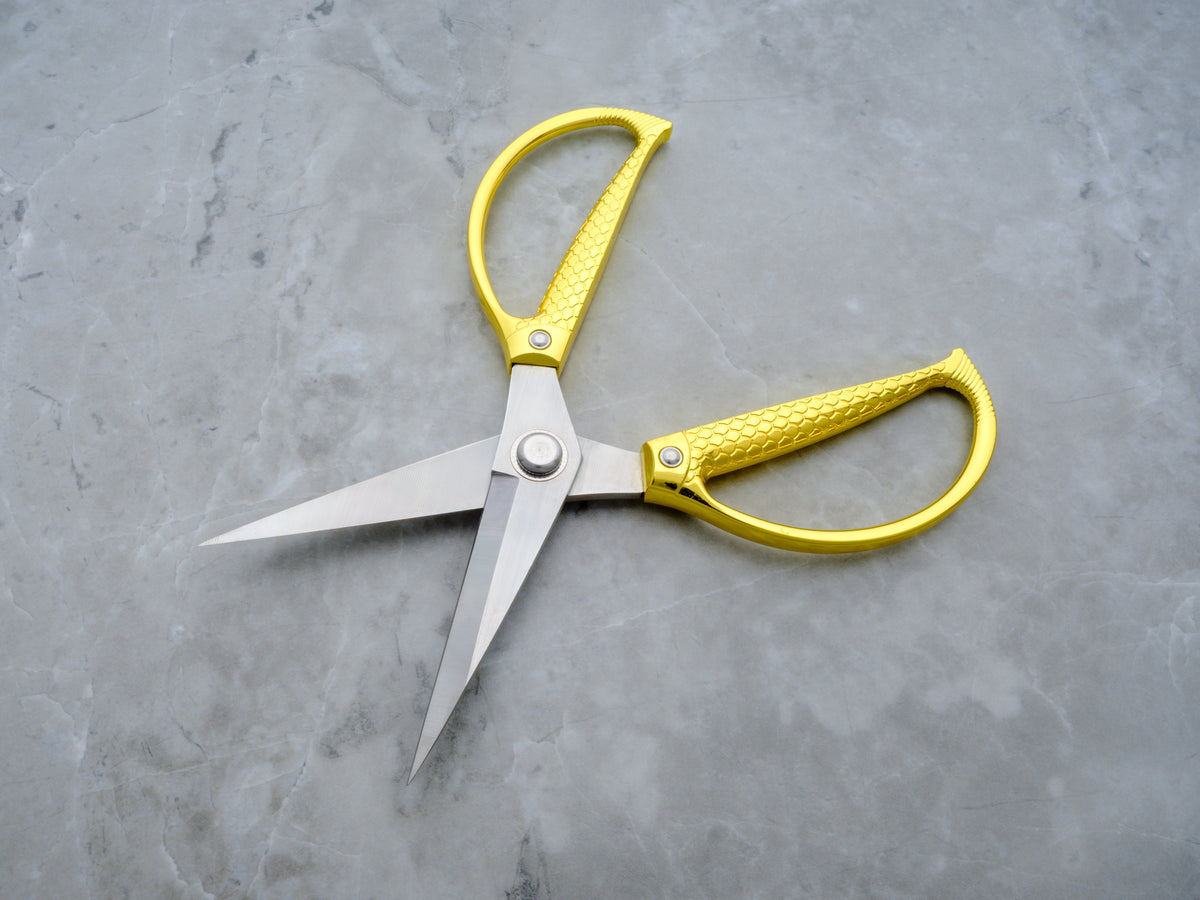 Gold handles with a snake scale print on XL stainless steel utility scissors. Set on a gray marble background.