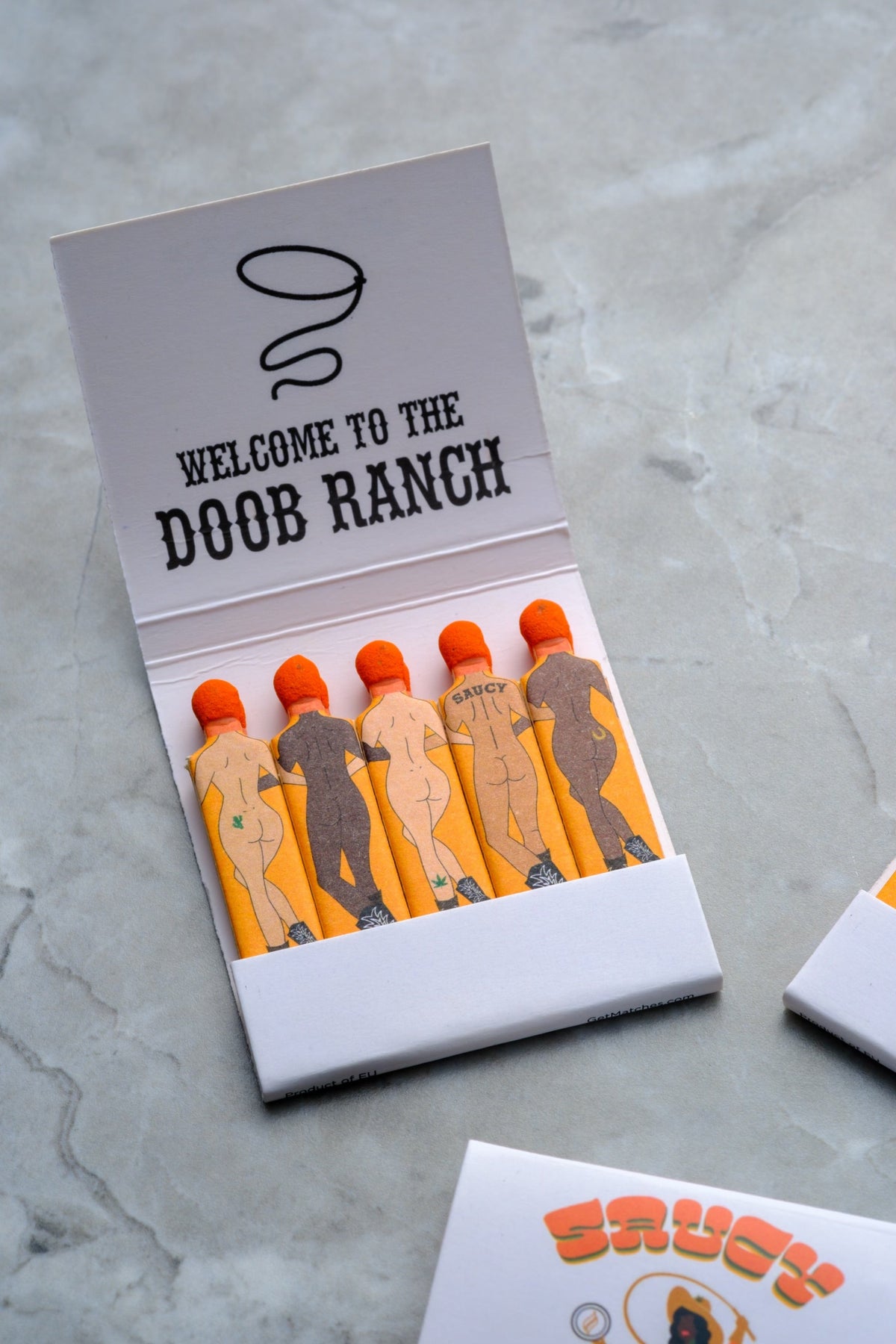Close up of Send Nudes Doob Ranch matches focusing on small cowboy and cowgirl figures. These matches are perfect for gifting and for elevating your ritual.