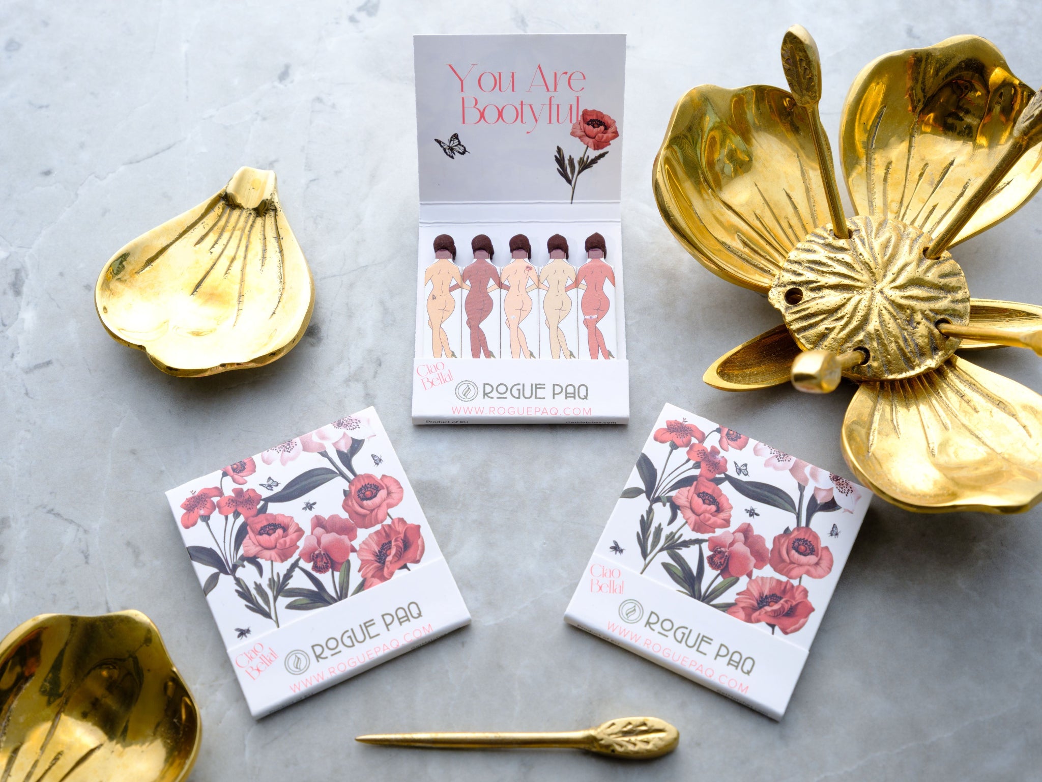 Open book of Rogue Paq safety matches featuring individually printed decorative stems for an elevated and detailed lighting experience; also featuring the Poppy brass ashtray
