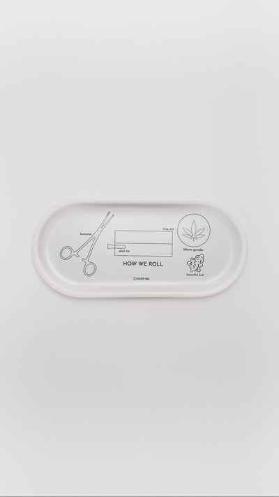 Close-up of the 'How We Roll' porcelain valet tray showing step-by-step black line illustrations of hands rolling a joint; a functional and artistic guide for the modern smoker.