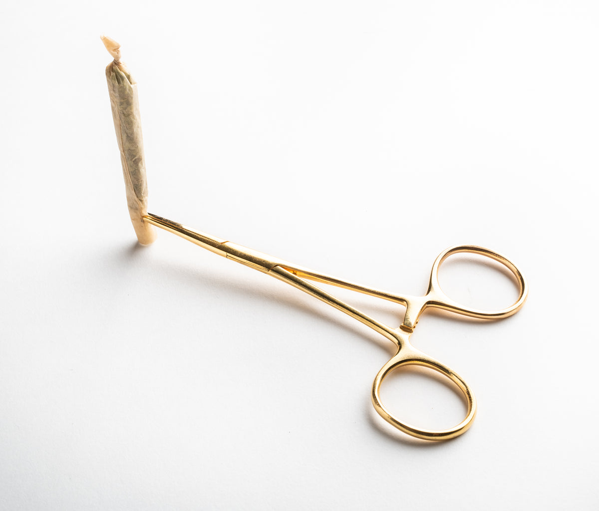 A sophisticated lifestyle shot featuring a hand-rolled joint made with Rogue Paq hemp papers, held by a pair of elegant gold-toned hemostats. This highlights the elevated, refined experience of using premium, natural materials.