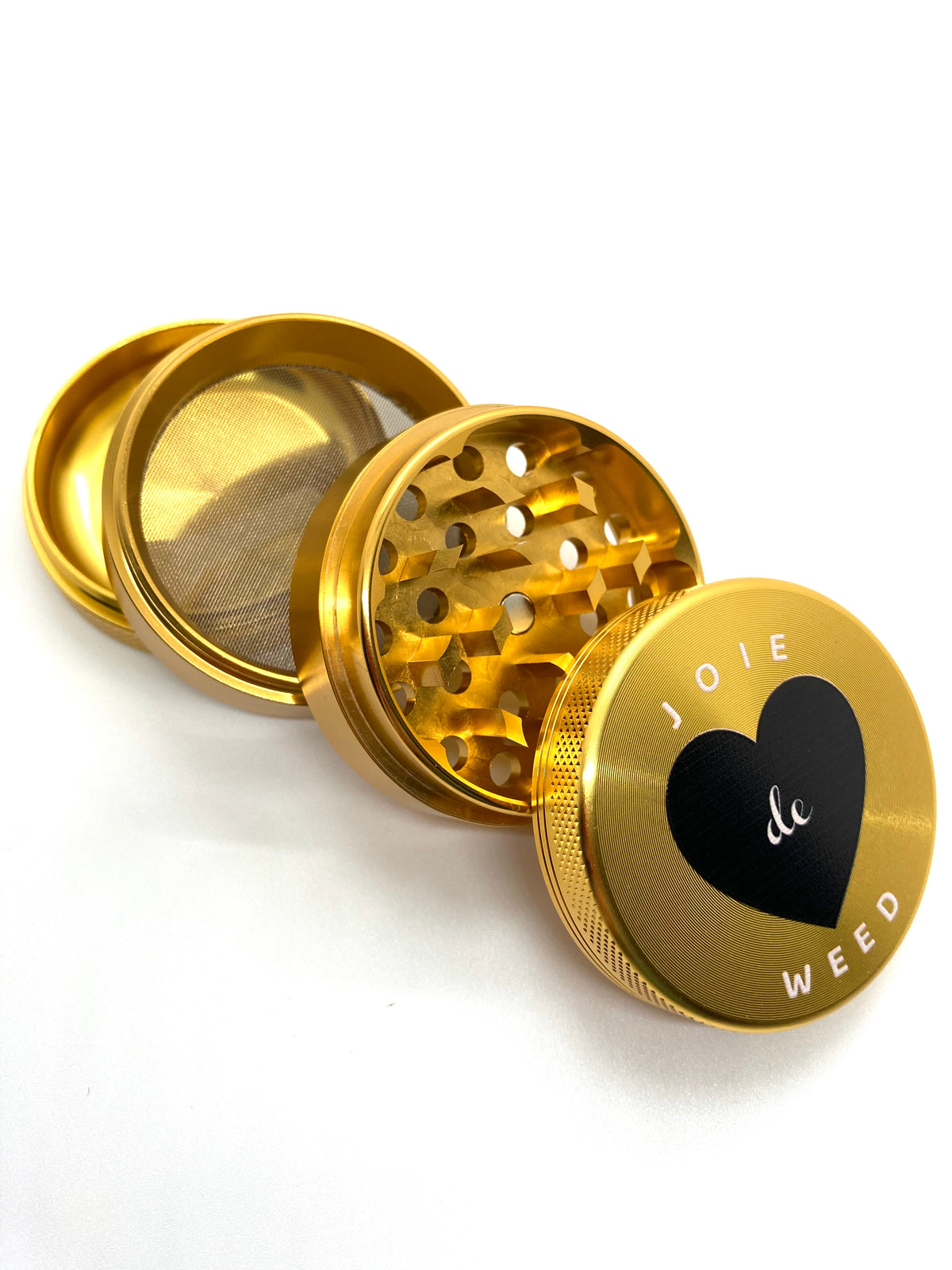 The 4-piece Joie de Weed grinder shown with its included triangular scraper tool. The set is presented as a professional-grade tool for the discerning smoker, designed to elevate the daily ritual with both function and style.