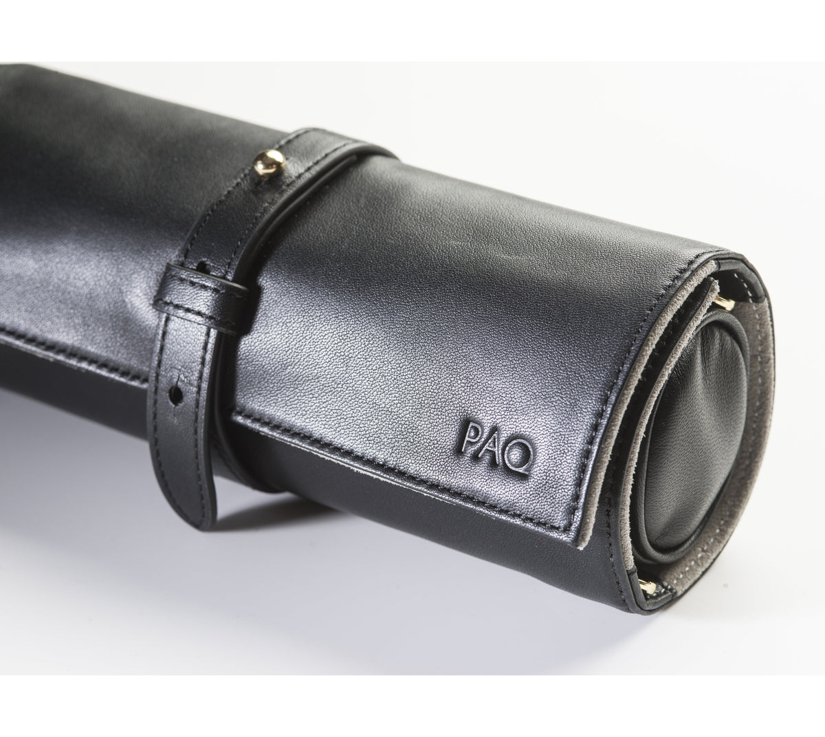 A close-up of a custom monogram debossed into the fine-grain black leather. The three gold-pressed letters 'PAQ' illustrate the personalization service, adding a bespoke and professional touch to the luxury carrier.