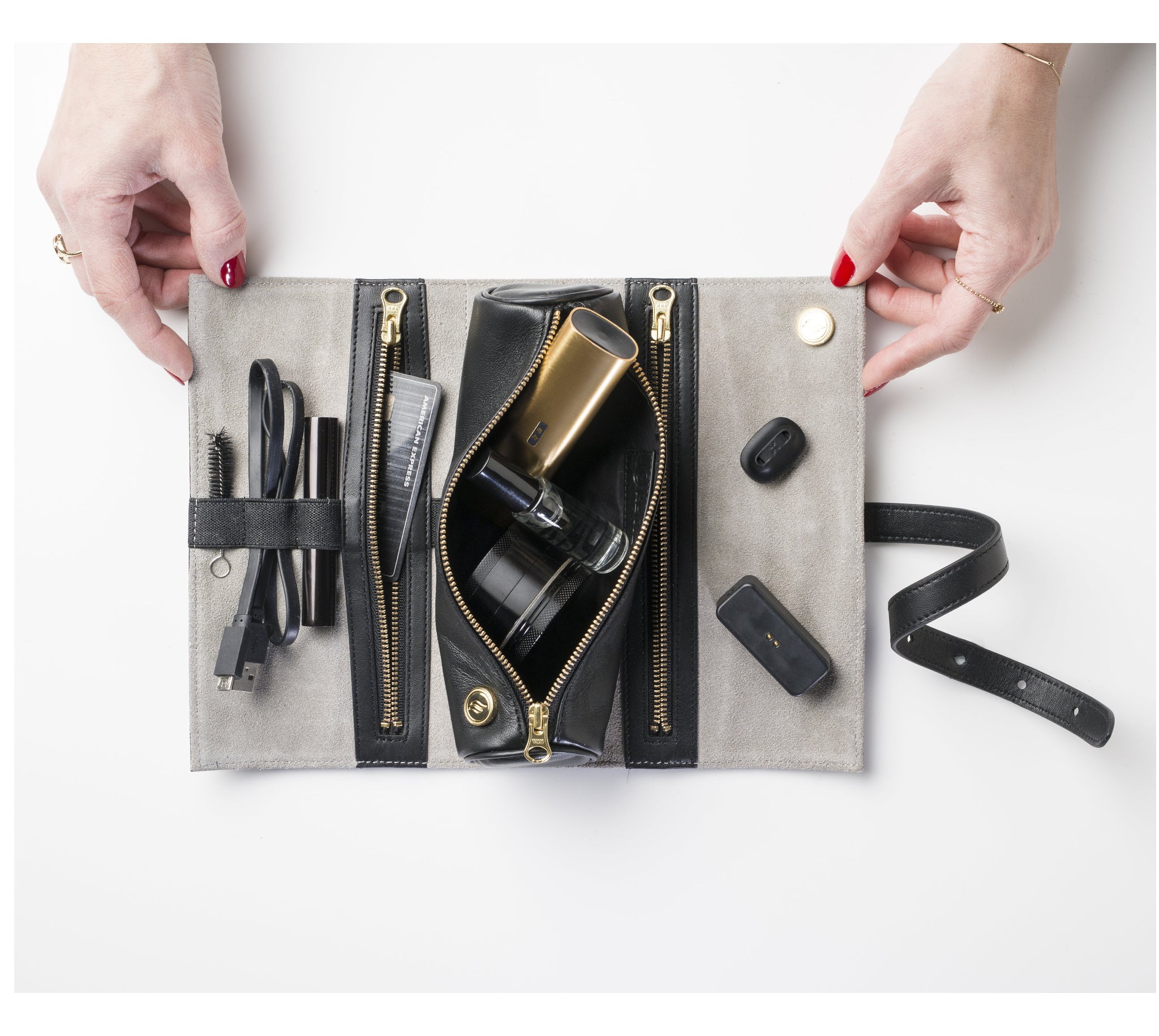 A woman's hands for scale holding the open Ritual Case. Inside are gold-toned accessories and other essentials secured by internal elastics of the unrolled Ritual Case. This lifestyle shot emphasizes the ease of use and the sophisticated, orderly nature of the Rogue Paq system.