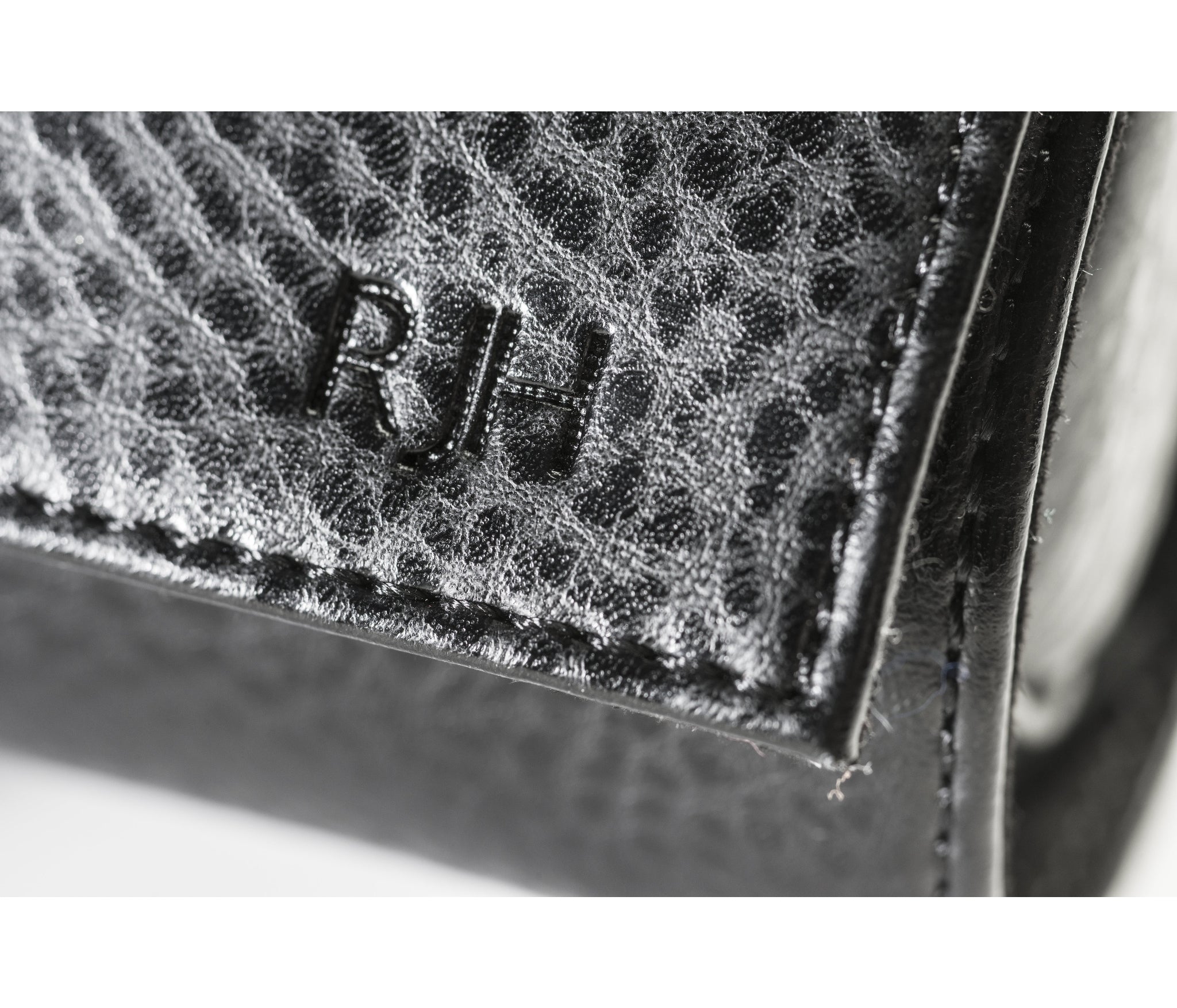 A close-up of a hand-pressed monogram on the corner of the vegan leather case. The image showcases the custom personalization option, where up to six capital letters are hand-pressed into the pebbled surface for a bespoke touch.